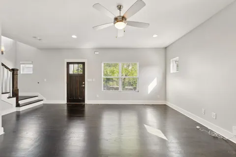 an empty room with wooden floor a chandelier fan and windows