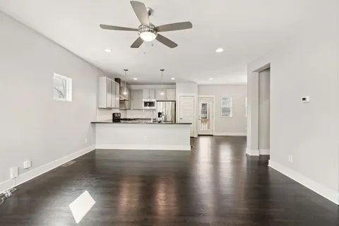 a view of an empty room and kitchen with wooden floor