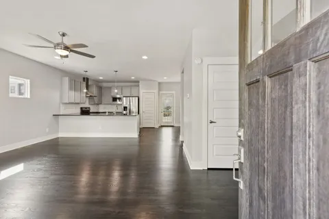 a view of an empty room and kitchen with wooden floor