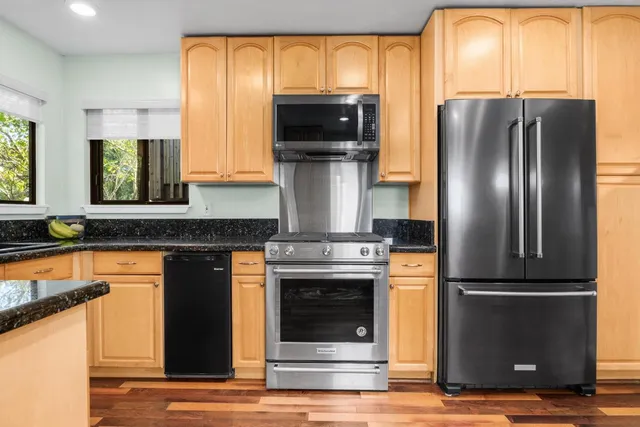 a kitchen with stainless steel appliances granite countertop a refrigerator a stove and a sink with wooden floor