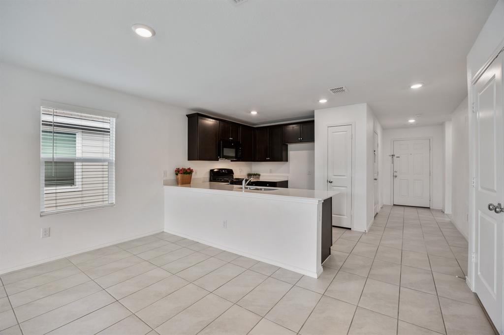 6038 Determine Lane Forney, TX 75126 - Photo 13 of 26 Open-concept living space with light-toned tile flooring, recessed lighting, and a kitchen featuring dark wood cabinetry, white countertops, and a built-in breakfast bar