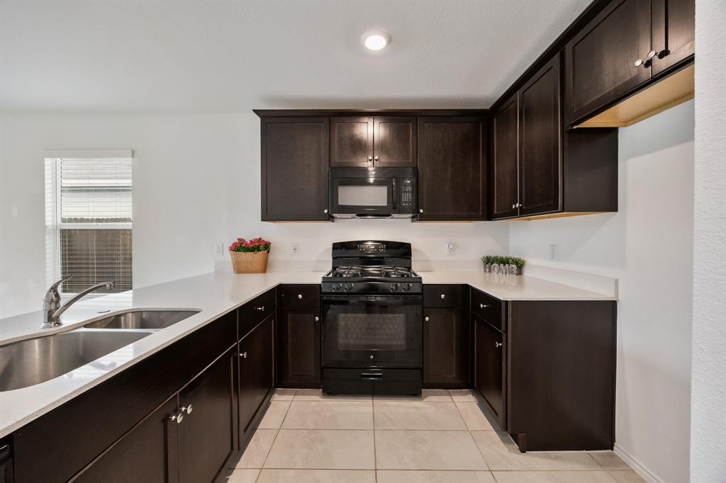 6038 Determine Lane Forney, TX 75126 - Photo 6 of 26 U-shaped kitchen featuring dark wood cabinetry, light-toned countertops, a black appliance suite with gas range and microwave, a double stainless steel sink with a chrome faucet, and tile flooring