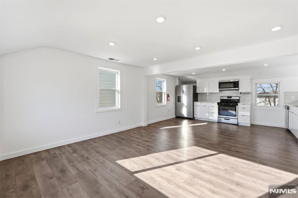 73 MacArthur Avenue Lodi, NJ 07644 - Photo 16 of 46 an empty room with wooden floor and kitchen view