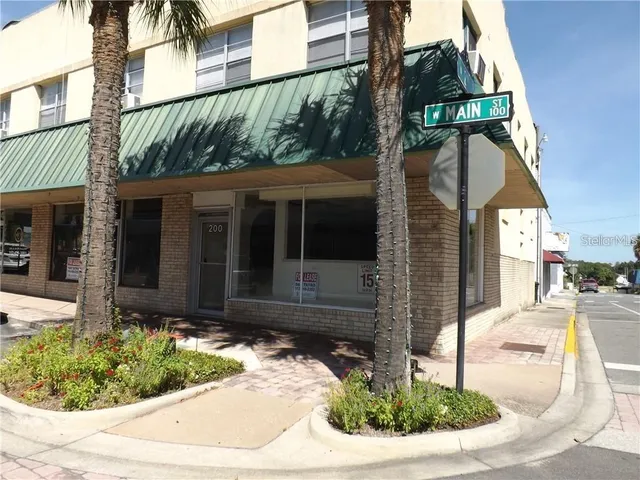 a view of brick house with a small yard plants and large tree