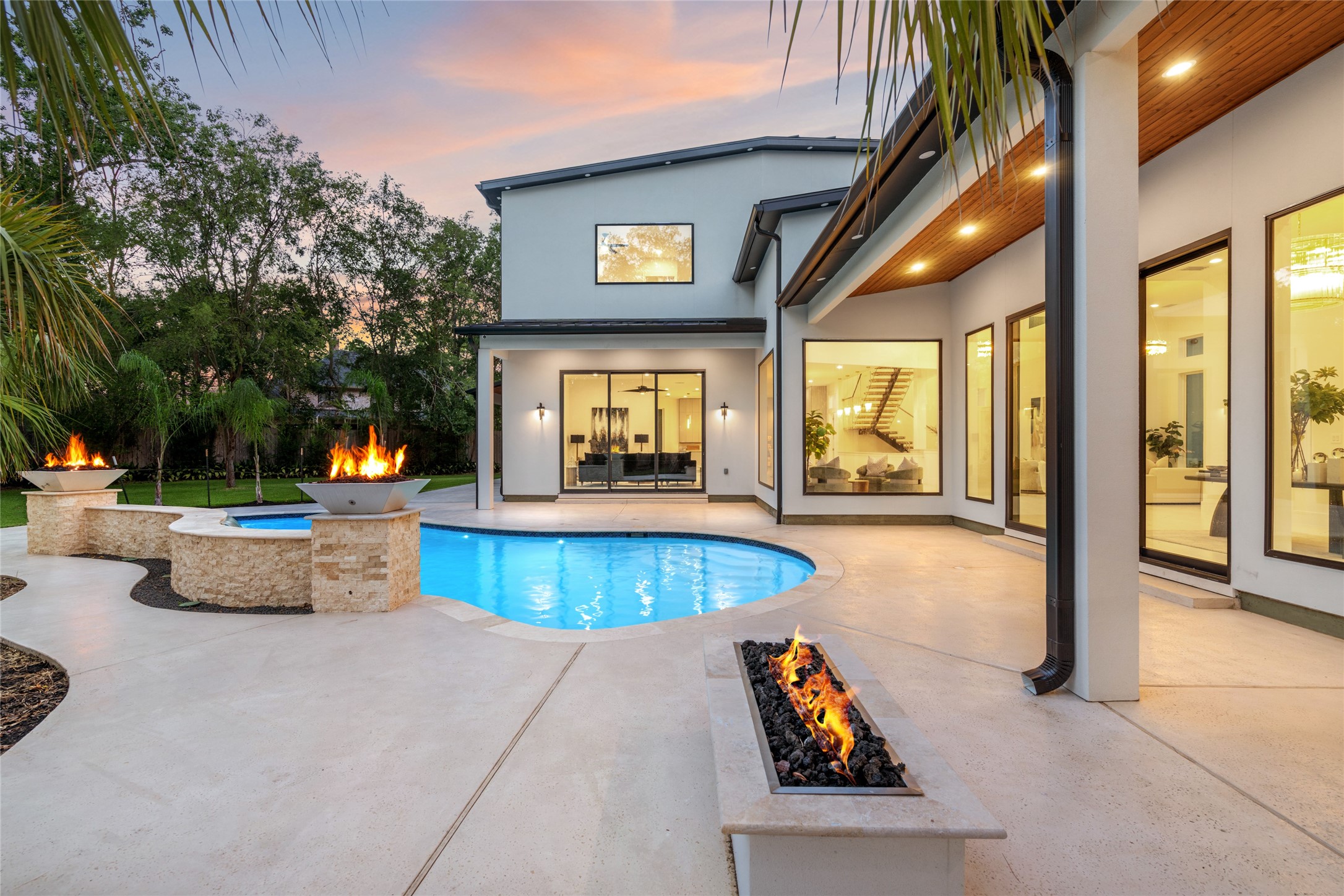 625 Piney Point Road Houston, TX 77024 - Photo 3 of 47 The back of the home is designed for effortless outdoor living, featuring an expansive covered patio with a warm pine-accented ceiling. Just off the primary suite, a sleek linear fire pit offers a private retreat, while the sparkling pool is framed by two dramatic fire bowls