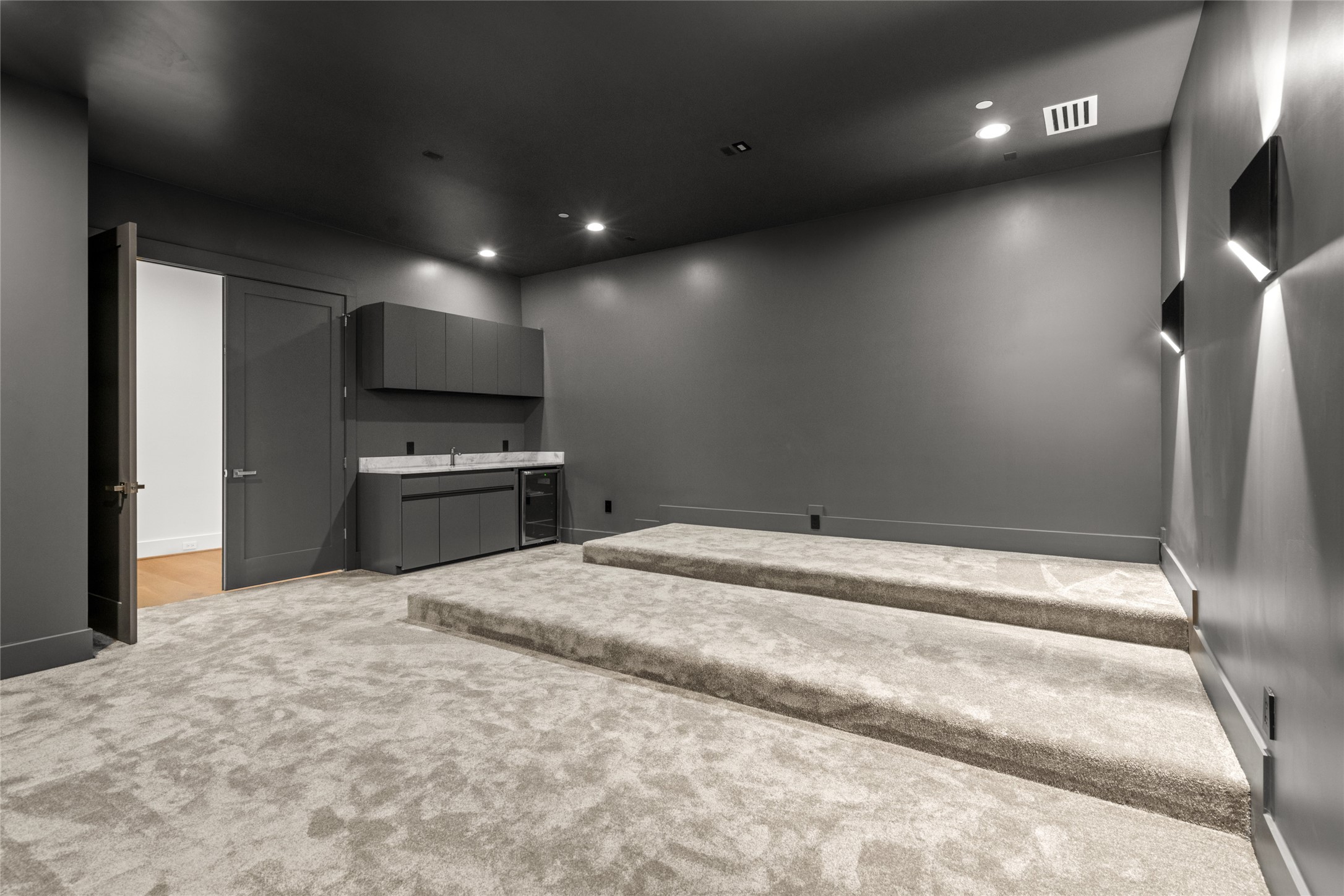 625 Piney Point Road Houston, TX 77024 - Photo 34 of 47 Movie night at its finest—this tiered-floor media room is built for comfort, with plenty of room for oversized seating, ambient wall-mounted lighting, and charcoal gray walls for a true theater feel. With no windows and a built-in bar featuring a quartzite countertop, storage, and beverage fridge, it’s designed for the ultimate at-home viewing experience.