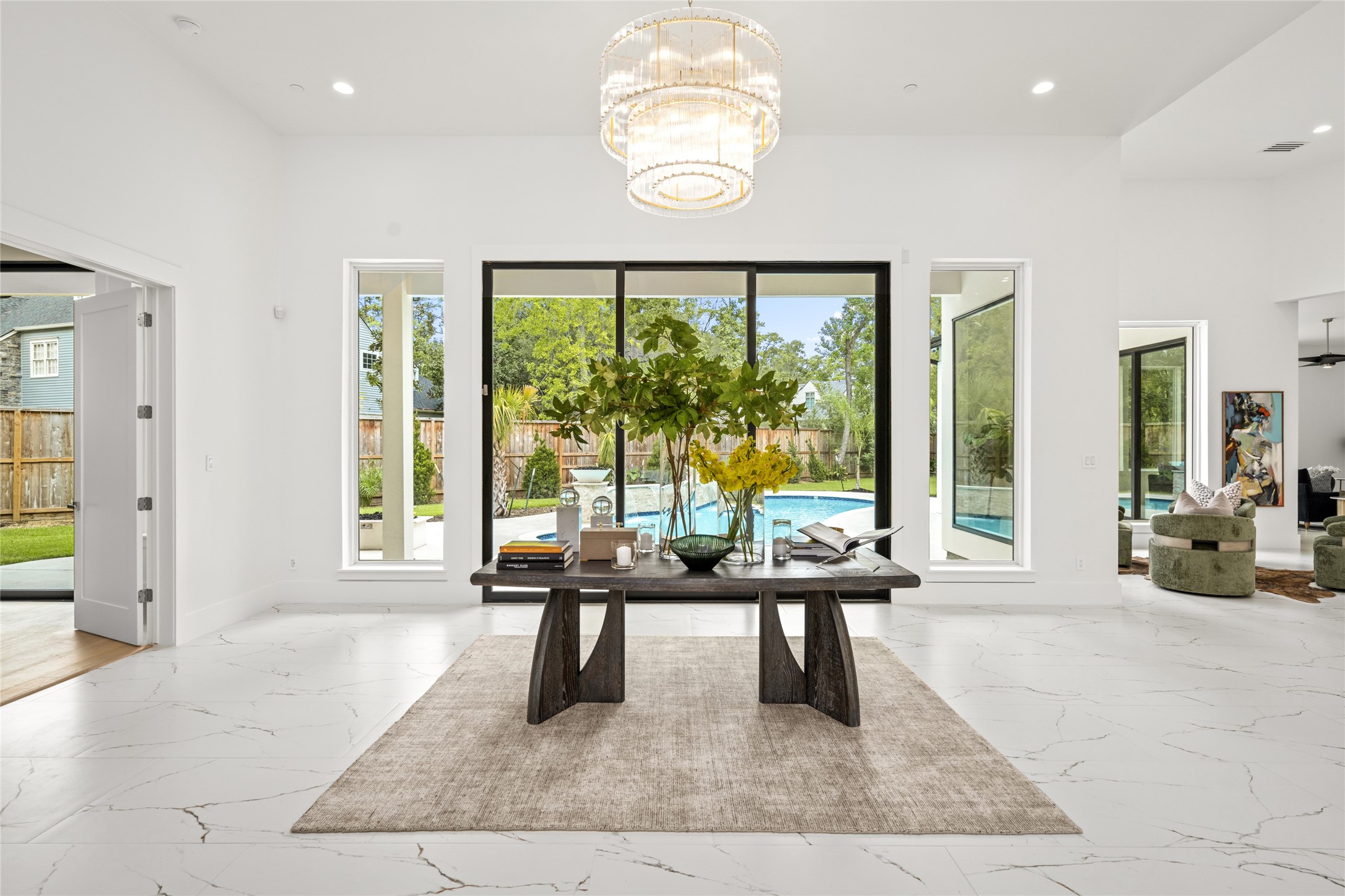 625 Piney Point Road Houston, TX 77024 - Photo 6 of 47 Entering through grand double iron and glass doors, you're welcomed into a spacious foyer with soaring 13-foot ceilings. Expansive floor-to-ceiling sliding glass doors showcase the sparkling pool beyond, while a striking three-tiered gold and crystal chandelier brings a modern touch of glamour.