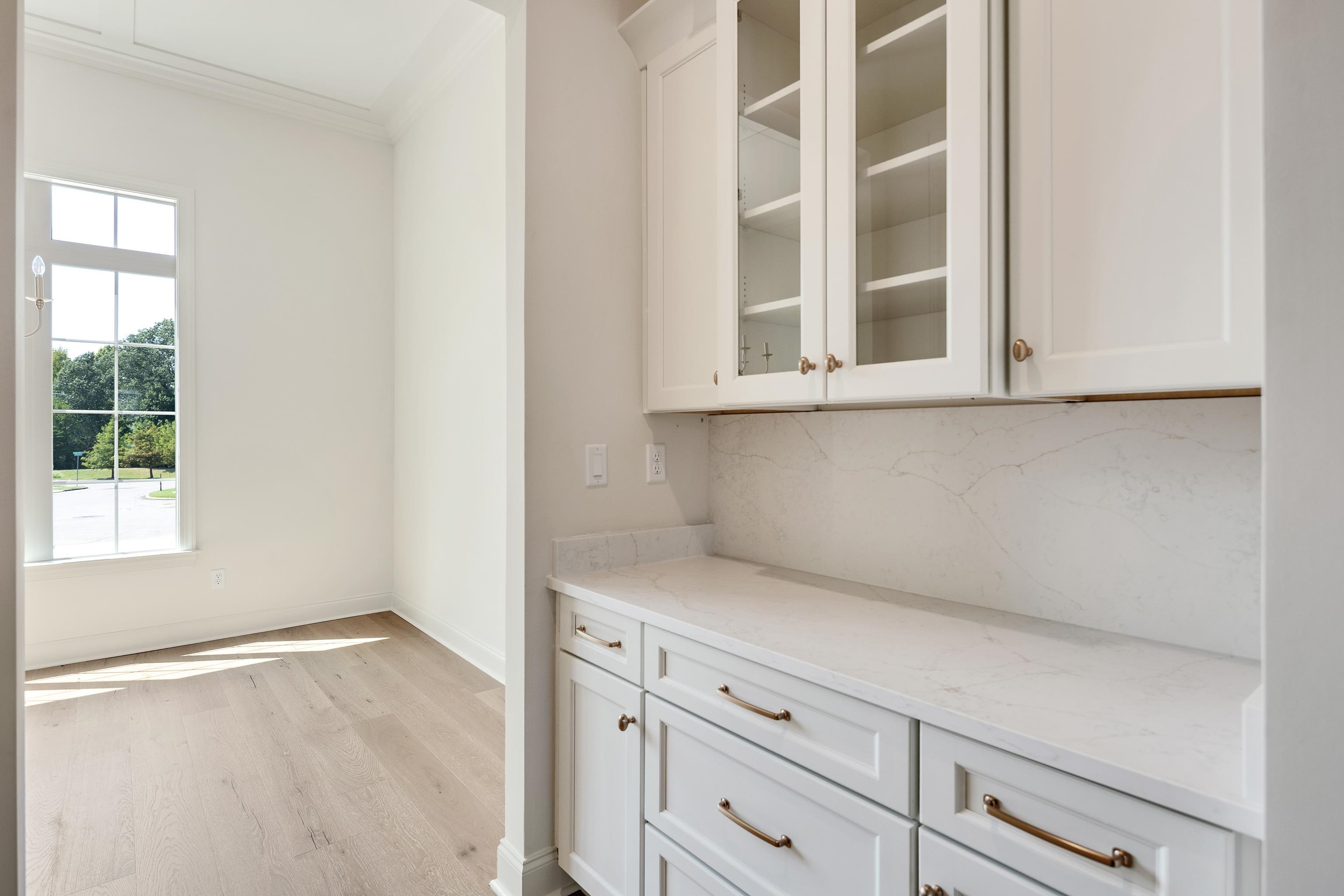 White cabinetry with glass-front upper cabinets, light-toned countertops, and brass-finish hardware