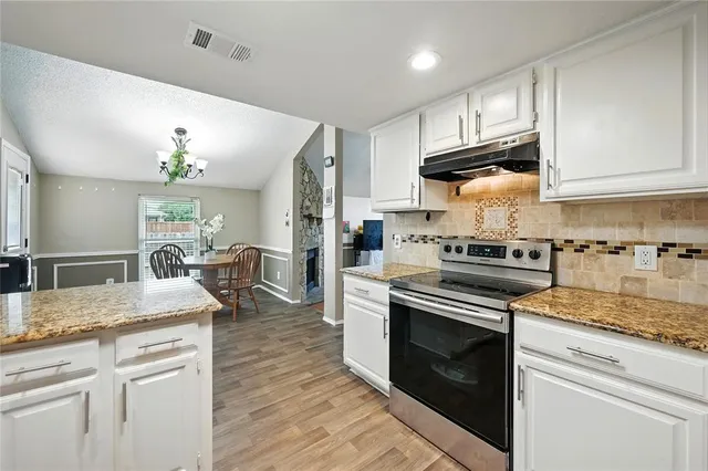a kitchen with granite countertop wooden floor stainless steel appliances and white cabinets