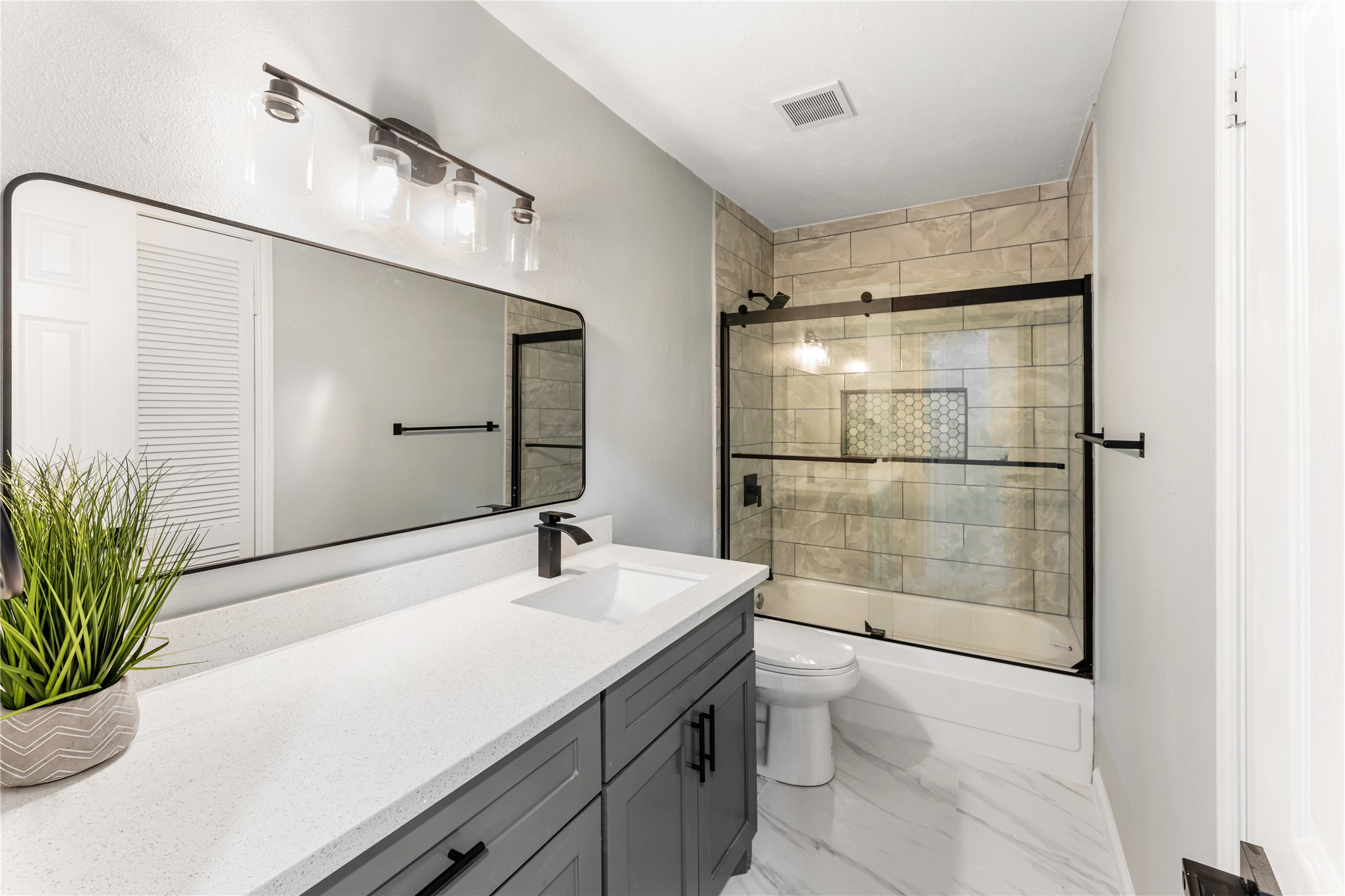 9425 Fondren Road Houston, TX 77074 - Photo 22 of 29 The stylish main bathroom features a sleek vanity with a quartz countertop, a large framed mirror, modern light fixtures, and a tiled shower with a glass door. The neutral color palette and clean lines create a sophisticated and welcoming space.