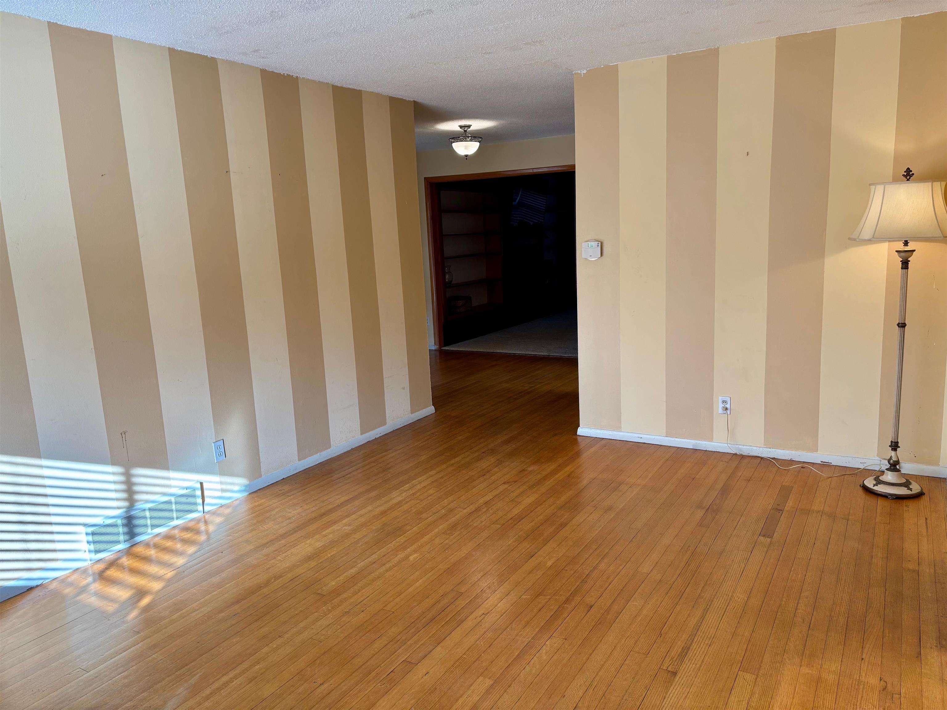 496 Chalmers Road Memphis, TN 38120 - Photo 5 of 20 Unfurnished room featuring baseboards, a textured ceiling, hardwood / wood-style flooring, and wallpapered walls