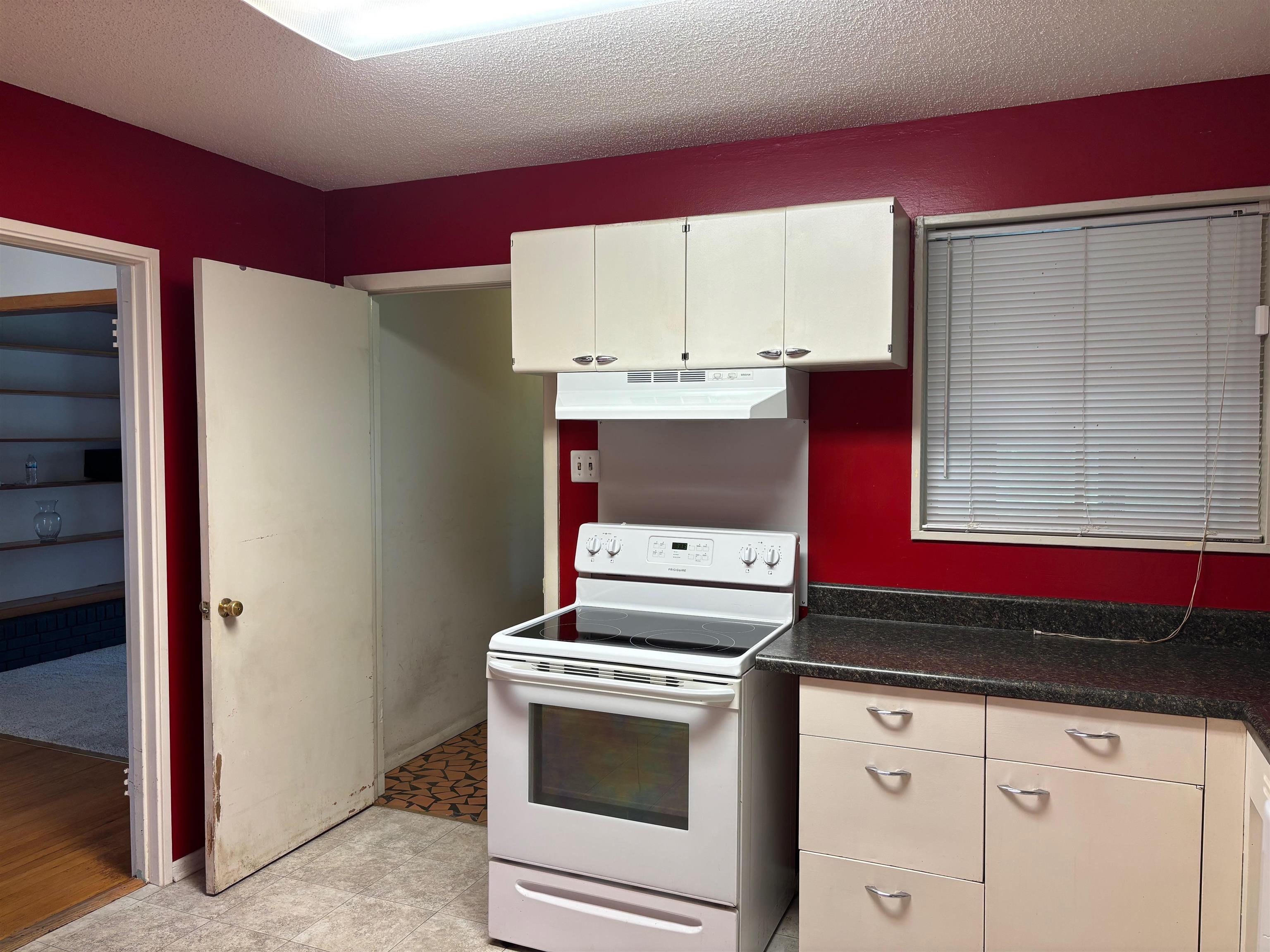 496 Chalmers Road Memphis, TN 38120 - Photo 8 of 20 Kitchen with a textured ceiling, dark countertops, white electric range oven, under cabinet range hood, and white cabinetry