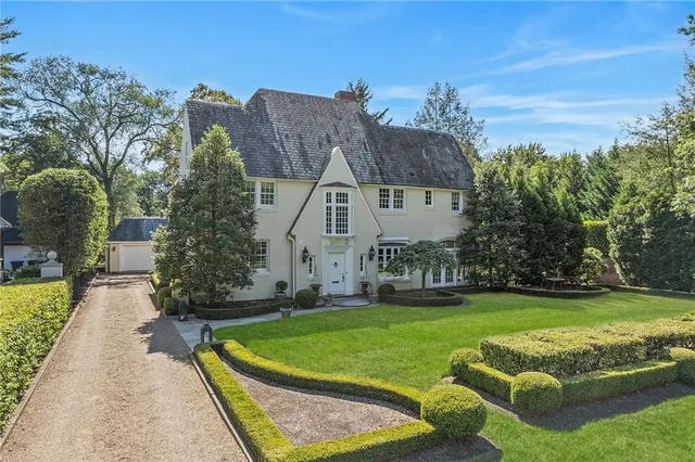 a view of a white house in a big yard with plants and large trees