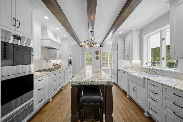 a large kitchen with stainless steel appliances granite countertop a large stove a sink dishwasher and white cabinets with wooden floor