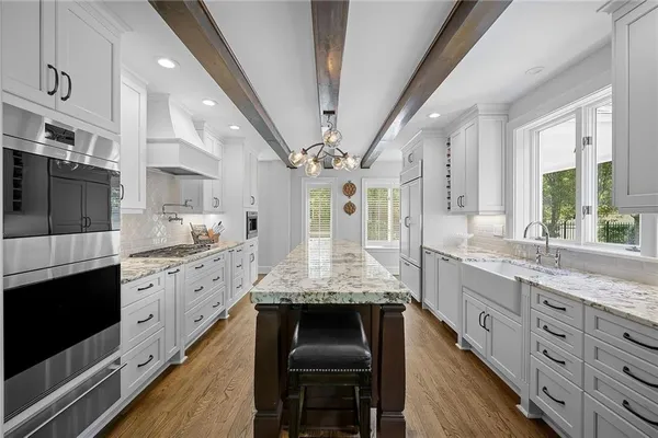 a large kitchen with stainless steel appliances granite countertop a large stove a sink dishwasher and white cabinets with wooden floor