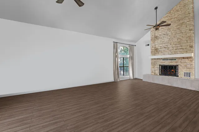an empty room with wooden floor fireplace and windows