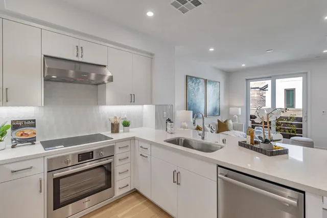 a kitchen with a sink dishwasher a stove and white cabinets with wooden floor