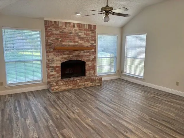 a view of an empty room with wooden floor fireplace and a window