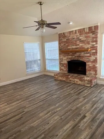 an empty room with wooden floor a fireplace a ceiling fan and windows
