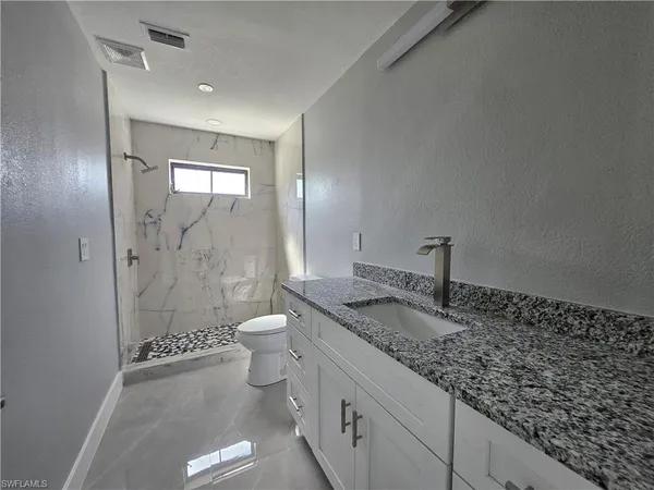 a bathroom with a granite countertop sink a toilet and shower