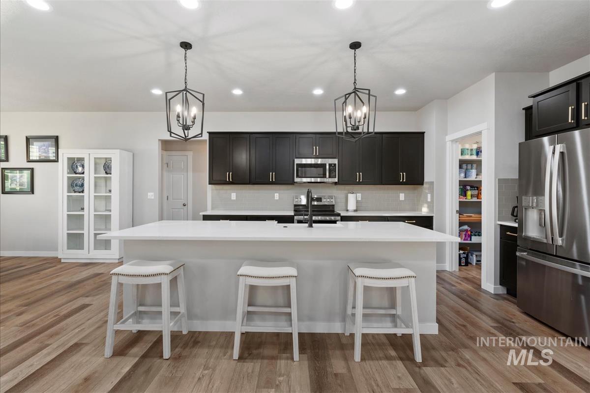 15451 Lutsen Avenue Caldwell, ID 83607 - Photo 12 of 39 Modern kitchen featuring a large central island with a solid surface countertop, wood-finish flooring, dark cabinetry, and stainless steel appliances