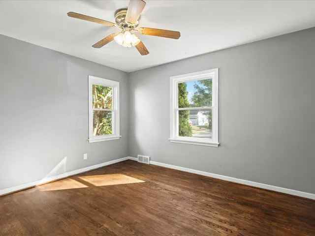 an empty room with wooden floor closet and windows