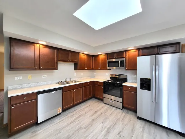 a kitchen with stainless steel appliances granite countertop wooden cabinets a refrigerator a sink a stove a microwave and wooden floors