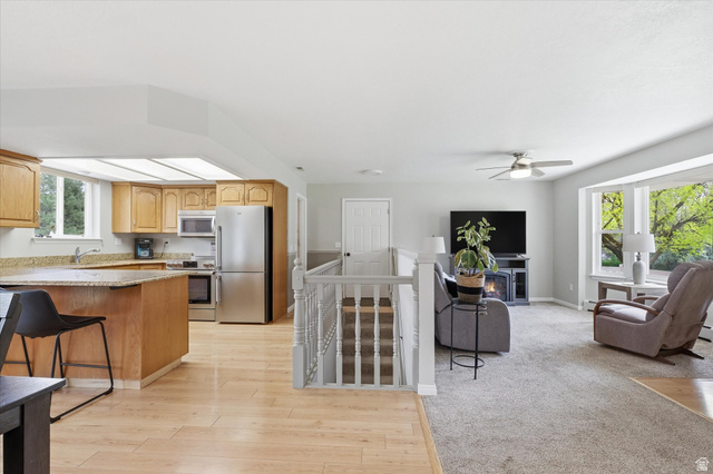 45 West 100 South Mendon, UT 84325 - Photo 14 of 64 Kitchen with stainless steel appliances, light wood-type flooring, a ceiling fan, light stone counters, and a breakfast bar