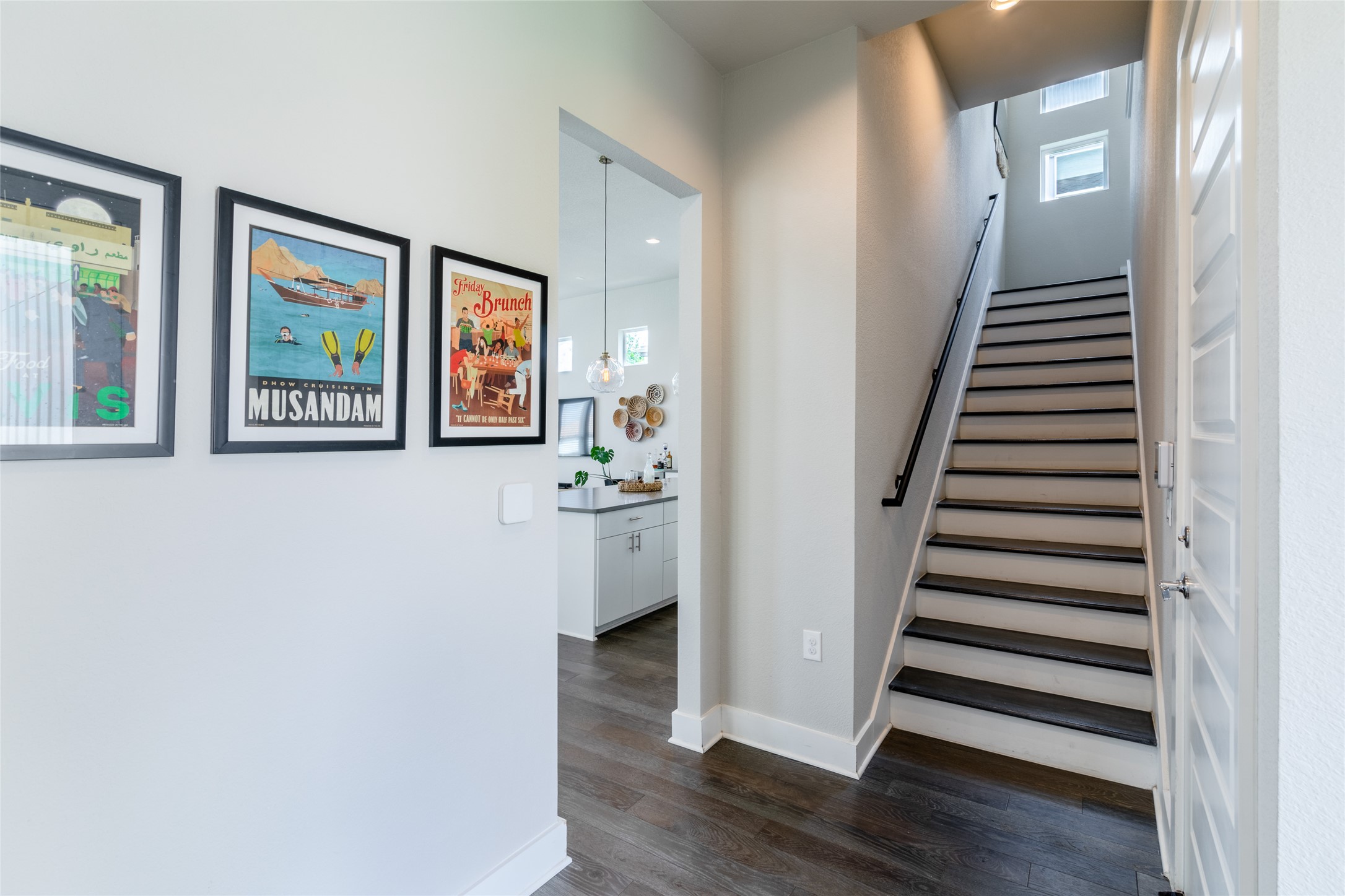6025 Seville Drive Austin, TX 78724 - Photo 29 of 40 Entryway featuring a dark wood-finish flooring, a contemporary staircase with black treads and white risers, handrail, and high windows for natural light with hallway view of the kitchen