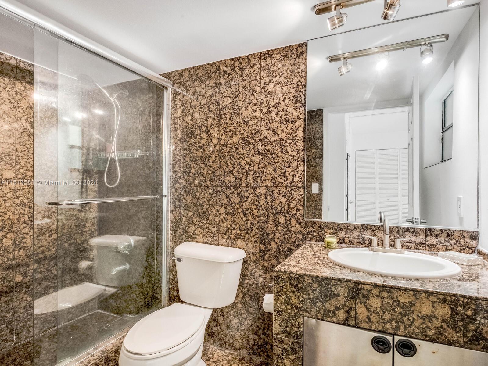 2430 Brickell Avenue, Unit 105A Miami, FL 33129 - Photo 22 of 27 a bathroom with a granite countertop sink toilet mirror and shower