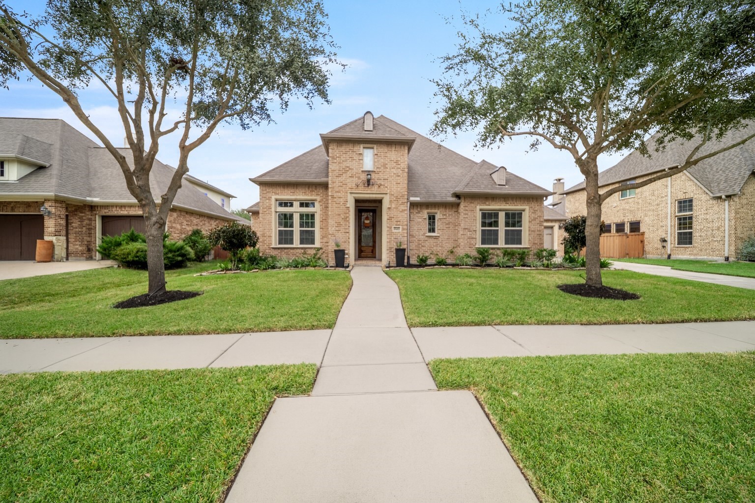 This is a charming brick home with a well-maintained front yard and a welcoming walkway leading to the entrance. Flanked by mature trees, the house features large windows, a pitched roof, and is situated in a peaceful neighborhood setting.