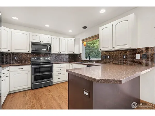 a kitchen with granite countertop a sink a stove a microwave a counter space and cabinets