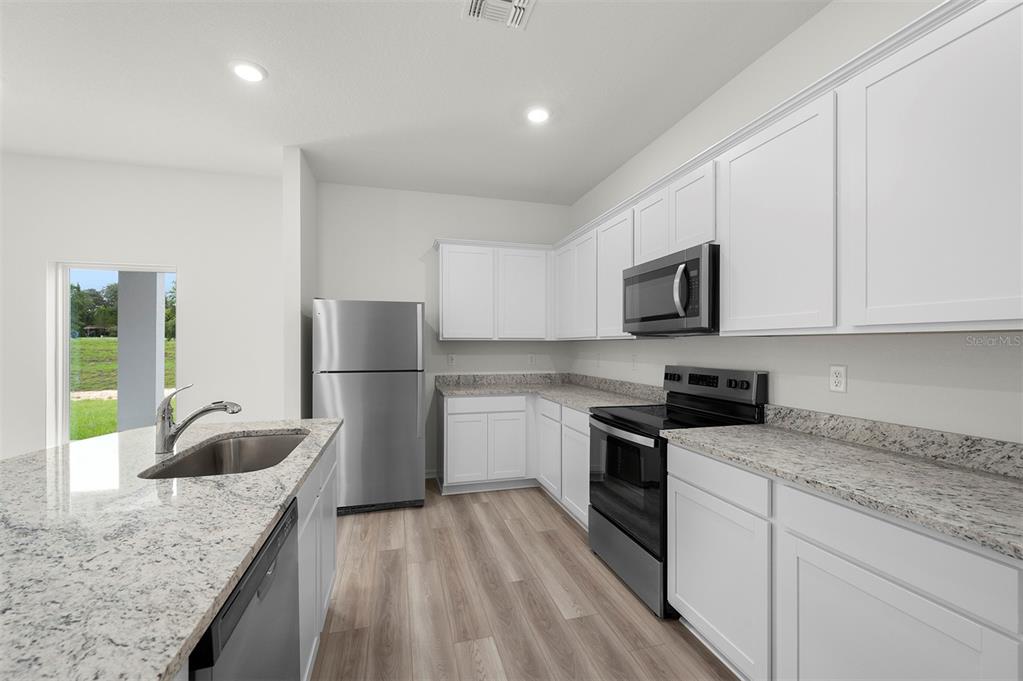 13291 Tula Loop Astatula, FL 34705 - Photo 6 of 22 a kitchen with granite countertop a sink a stove top oven a refrigerator and white cabinets