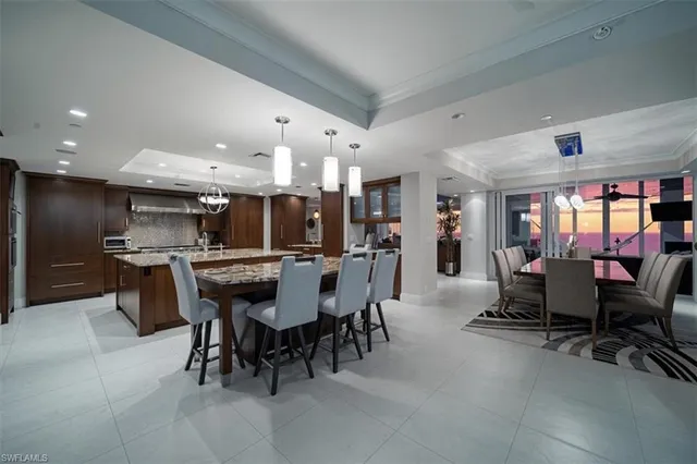 a kitchen with stainless steel appliances kitchen island granite countertop a dining table chairs and a refrigerator