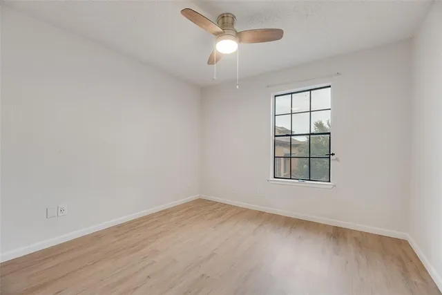 an empty room with wooden floor ceiling fan and windows
