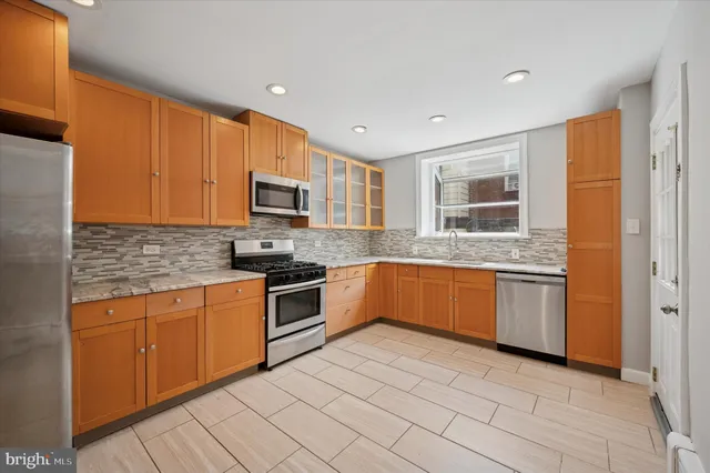 a kitchen with stainless steel appliances granite countertop a stove top oven a sink dishwasher and a refrigerator with wooden cabinets