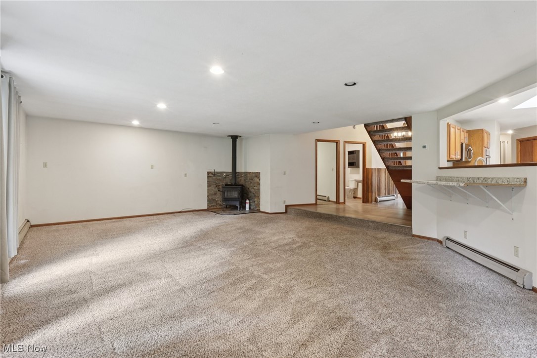 5643 Chapin Road Madison, OH 44057 - Photo 8 of 50 Unfurnished living room featuring baseboard heating, a wood stove, light colored carpet, stairs, and recessed lighting