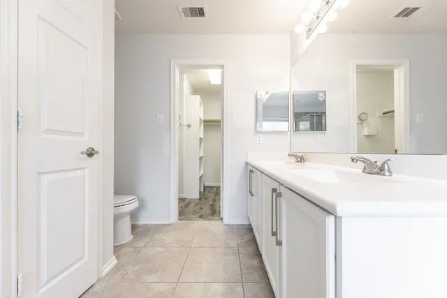 a spacious bathroom with a double vanity sink a toilet and a mirror