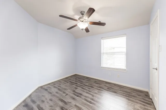 an empty room with wooden floor fan and windows
