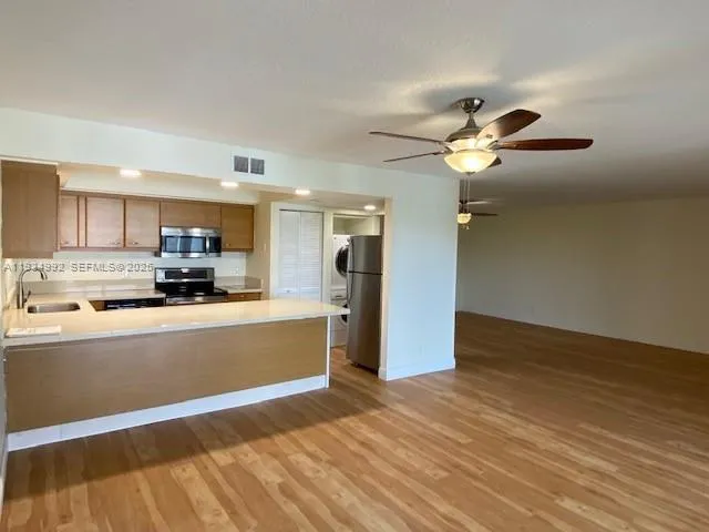 a view of a kitchen with a sink a refrigerator a ceiling fan and wooden floor