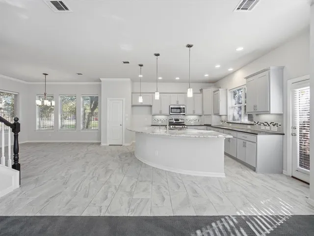 a large white kitchen with kitchen island a sink dishwasher a stove a refrigerator and white cabinets with wooden floor