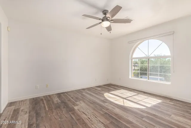 an empty room with wooden floor fan and windows