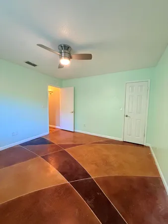 a view of an empty room with wooden floor and fan