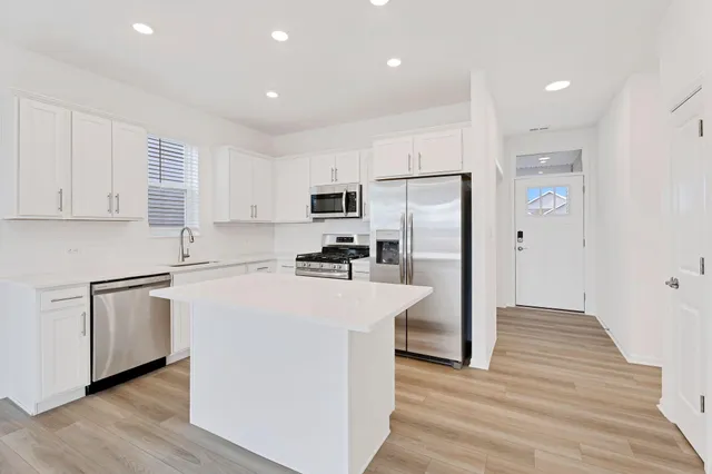 a kitchen with stainless steel appliances granite countertop a refrigerator a stove top oven a sink and dishwasher with wooden floor