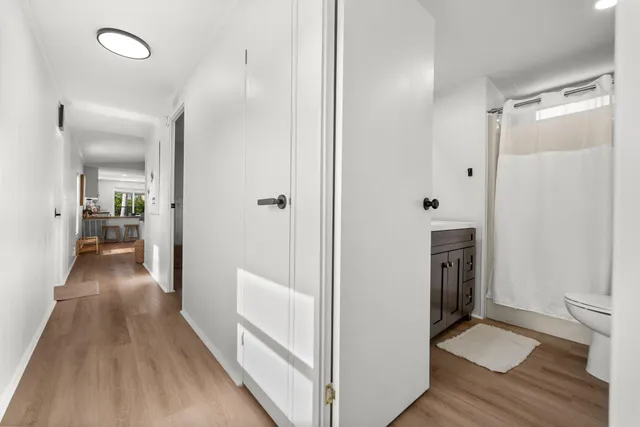 a view of a hallway with wooden floor and a bathroom