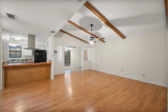 a view of empty room with wooden floor and kitchen
