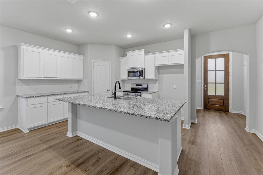 1329 Frio Drive Springtown, TX 76082 - Photo 9 of 25 Kitchen featuring a large island with a sink, stainless steel appliances, white cabinetry, granite countertops, and wood-finish flooring