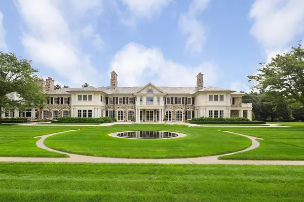 a front view of a white building with a garden and trees