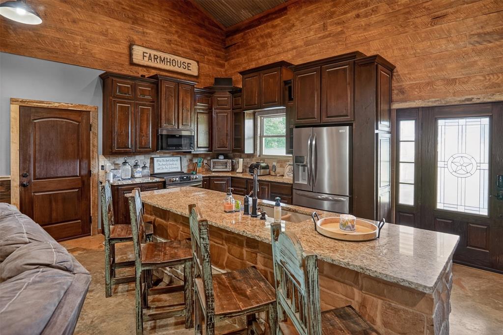1524 County Road Sumner, TX 75486 - Photo 12 of 35 Kitchen featuring a stone-clad island with a granite countertop, dark wood cabinetry, and stainless steel appliances