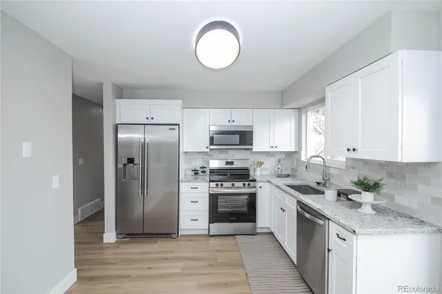 a kitchen with stainless steel appliances granite countertop a stove a sink dishwasher a refrigerator and a oven with wooden floor